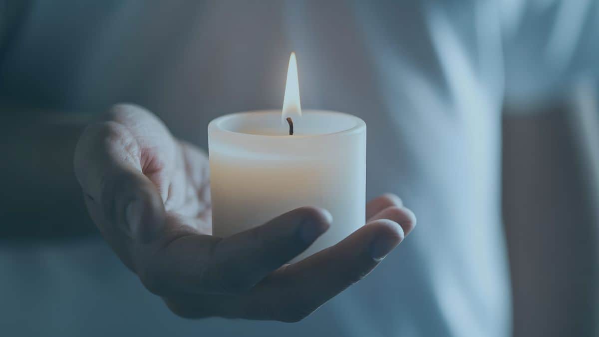 Man holding out his hand cupping a single lit candle, symbolizing grief and healing.
