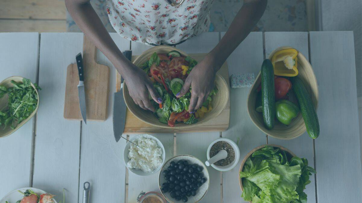 Woman making a salad in a wooden bowl with healthy ingredients , symbolizing the need for essential nutrients when the impact of stress and grief is felt on the body.